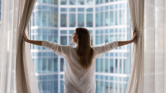 woman drawing back the curtains of her home